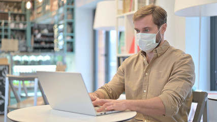 Young Man with Face Mask using Laptop in Cafe