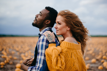 A young woman leaned against her husband's back while standing in a pumpkin field.