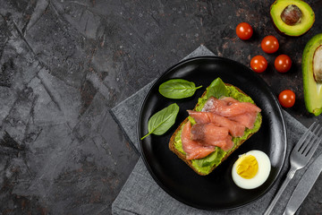 Sandwich with salmon on a black plate. Fish fast food on a black table.