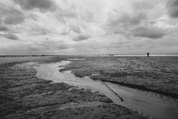 Black and white clouds over the beach with winding water leading to the North Sea