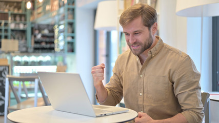 Obraz premium Young Man Celebrating Success on Laptop in Cafe