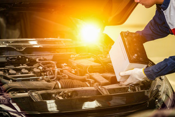 Male mechanic changing car battery, engineer is replacing car battery because car battery is...