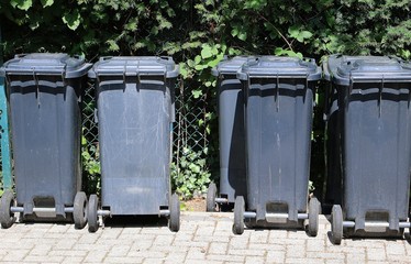 dark garbage cans are standing at the fence in a row