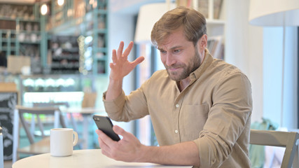 Disappointed Man Reacting to Loss on Phone in Cafe