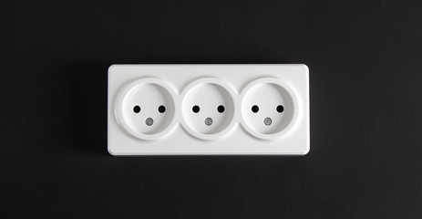 Light socket with three connectors on a black wall in a horizontal position.