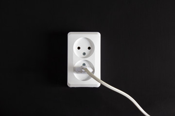 Socket with two plugs on a black wall with a plug in.