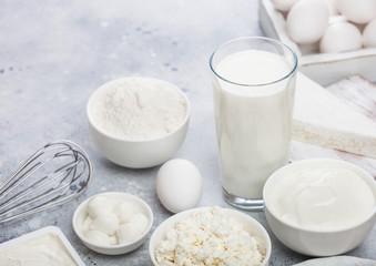 Fresh dairy products on white table background. Glass of milk, bowl of sour cream, cottage cheese and baking flour and mozzarella. Eggs and cheese. Steel whisk. Space for text