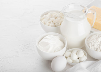 Fresh dairy products on white table background. Glass jar of milk, bowl of sour cream, cottage cheese and baking flour and mozzarella. Eggs and cheese.