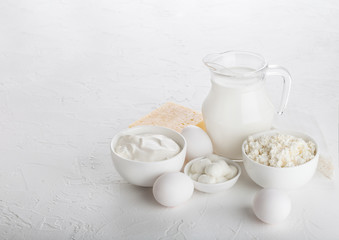 Fresh dairy products on white table background. Glass jar of milk, bowl of sour cream and cottage...