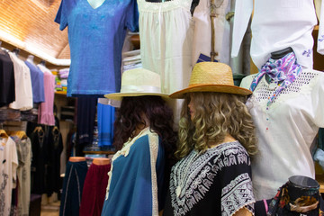 The front of a clothing store. Lifeless mannequins stand in the background in the store with various items. Close up.