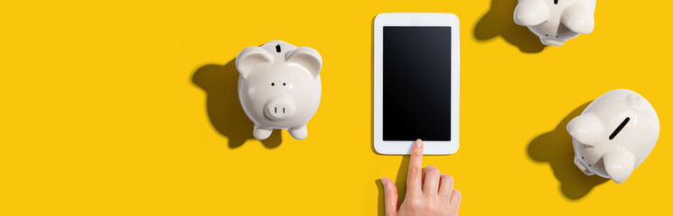 Person using a tablet computer with piggy banks from above