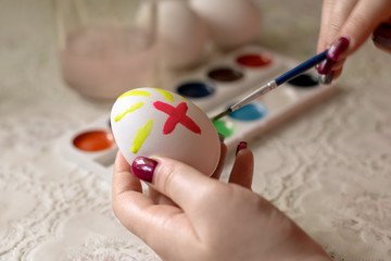Easter egg coloring. A woman paints with a brush on an egg. Red cross on an easter egg