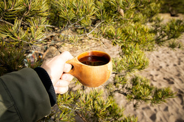 Hand holding hot tea cup at green blur pine tree branche, Leisure lifestyle.