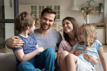 Close up of happy young mom and dad have fun playing with little kids relaxing on couch together, smiling young family parents sit on comfortable sofa rest enjoy weekend with children at home