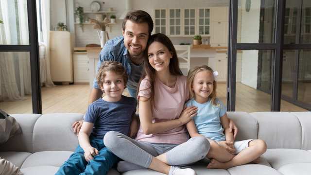 Portrait of happy successful young family with children first time home buyers sit on comfortable couch, smiling parents and little kids relax in living room look at camera posing, ownership concept