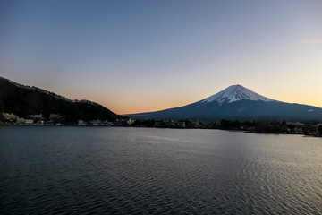 A view on Mt Fuji from the side of Kawaguchiko Lake, Japan. Soft colors of sunset - golden hour. Top of the volcano covered with a snow layer. Serenity and calmness. The lake's side is reed beds.