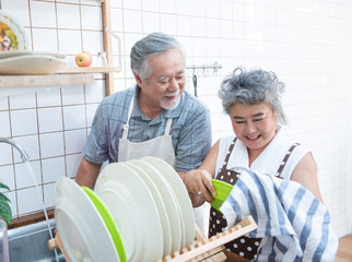 Happy asian elder senior couple washing dishes in sink at home in kitchen at home.