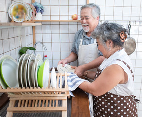 Happy asian elder senior couple washing dishes in sink at home in kitchen at home.