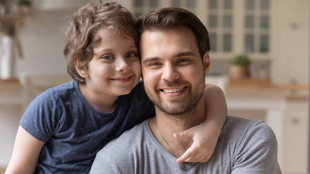 Close up portrait of smiling young father and preschooler son hug cuddle look at camera posing for family picture together, happy dad and cute little boy child embrace show support love and care
