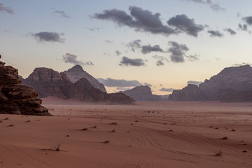 Fototapeta na wymiar Kingdom of Jordan, Wadi Rum desert, sunset winter day scenery landscape with white puffy clouds and warm colors. Lovely travel photography. Beautiful desert could be explored on safari. Colorful image