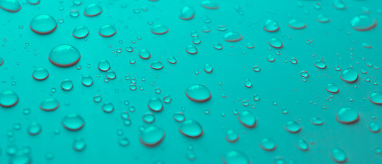 Many different drops of water rain on a turquoise background, close up