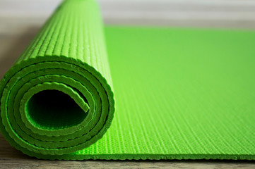 The yoga mat of green color lies on the floor. Healthy lifestyle. Light background, blur of the back and side plan.