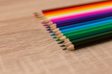 Fototapeta premium A number of colored pencils in a row on wooden background. Colorful photograpphy. Selected focus.