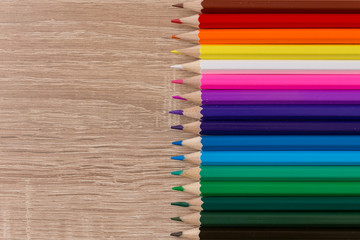 A number of colored pencils in a row on wooden background. Colorful photograpphy.