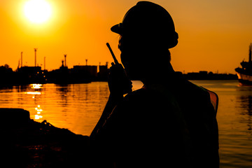 Sillhouette of an engineer or male technician, standing by the shipping port in her hand holding radio communication, to industry concept.