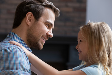 Naklejka premium Close up side view of happy young father and cute small daughter have fun playing together in princess girly game, smiling dad and little girl child entertain relax together on home weekend
