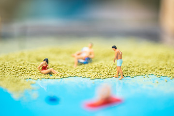 Fototapeta na wymiar Miniature people, travelers relaxing on the sand box decorating in summer theme using as background travel, exploring the world, budget trip concept.