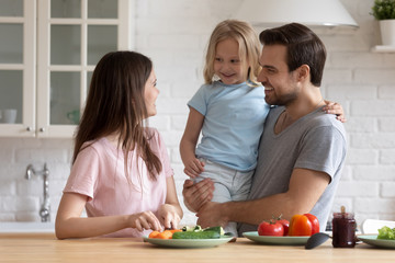 Obraz na płótnie Canvas Happy young family with small preschooler daughter have fun preparing breakfast or lunch in kitchen, smiling parents have fun with little girl child cook salad chop vegetables, healthy life concept