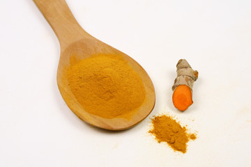 Turmeric powder in a wooden spoon and fresh turmeric roots isolated on a white background is an ingredient in turmeric foods and ingredients in skin care products. Turmeric helps the skin to be strong