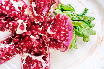 a red pomegranate cut into pieces is lying on a white plate decorated with mint sprigs.