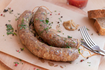 Homemade sausages on paper with mustard and tomato sauce. Cutlery and bread. Top view on a wooden background. Hands holding cutlery.