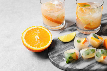 Ice cubes with orange and mint on light grey table