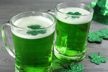 Green beer and clover leaves on grey wooden table, closeup. St. Patrick's Day celebration