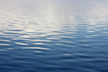 a soothing background with blue water of the river with small ripples and the reflected clouds