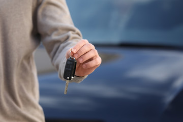 Man holding key in modern auto dealership, closeup. Buying new car
