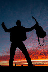 Silhouette of male musician standing, holding guitar on a scenic violet sunset sky 