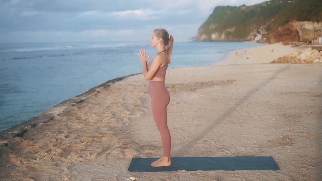 slim girl with ponytail does mountain yoga pose on beach