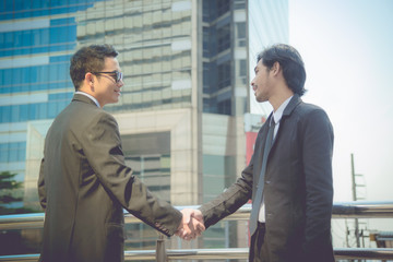 Two young businessmen shaking hands on overpass