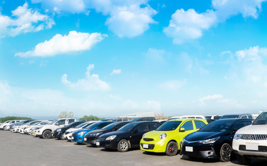 Car parked in large asphalt parking lot with white cloud and blue sky background.