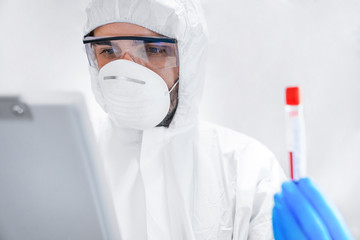 Scientist in chemical protective suit with test tube at laboratory making notes. Virus research