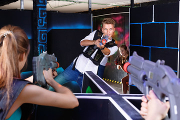 Two laser tag teams playing enthusiastically and aiming at each other in dark room