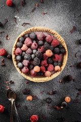 Healthy sweets concept. Delicious open pie with frozen raspberries, blackberries, currants and sugar icing served with dry hibiscus flowers on black background