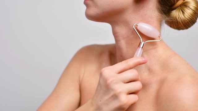 Woman is getting rejuvenation massage neck using jade face roller.