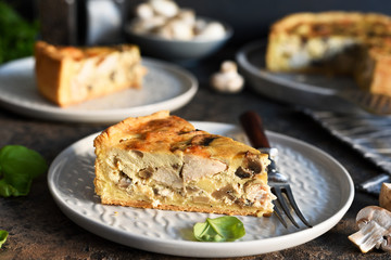 Tart slice on the kitchen table. Traditional quiche with chicken, mushrooms and cheese on a dark concrete background.