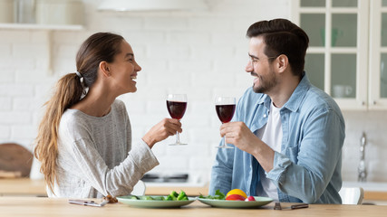 Smiling man and woman chatting, drinking red wine in modern kitchen, happy wife and husband holding...