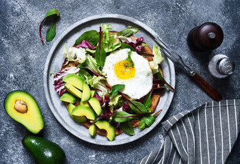 Classic breakfast - fried eggs, salad with avocado and bread toast on a concrete background.